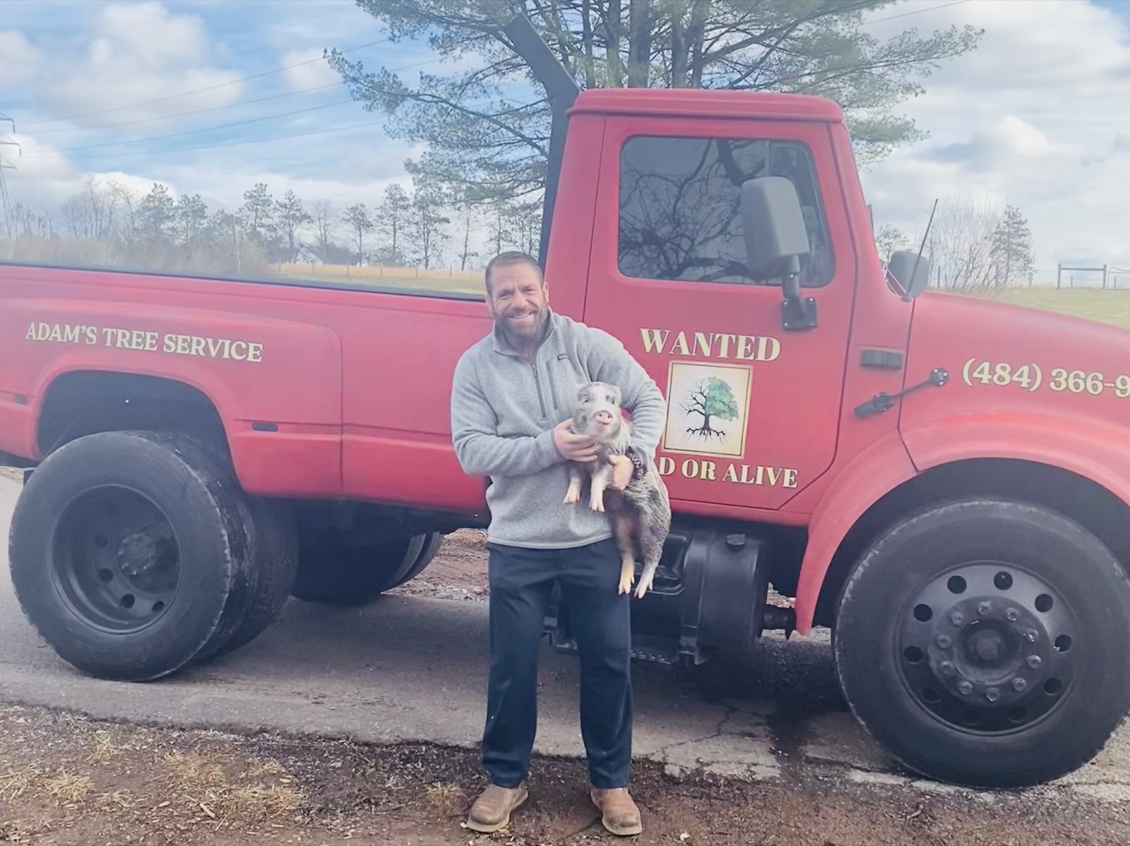 Adam holding a small pig in front of the red Adam's Tree truck